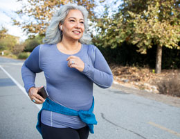 A woman carrying a phone jogs down a street.