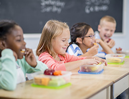 A row of kids eating out of lunch boxes. 