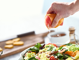 Someone is squeezing a lemon and juice is pouring onto a bowl of salad.