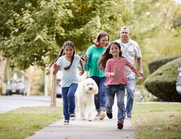  Two girls run down the sidewalk in front of a man, woman and leashed dog.
