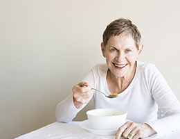 An older woman sits at a table eating.